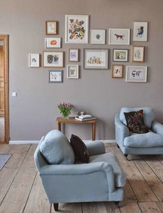 a living room with two blue chairs and pictures on the wall above them, along with a coffee table