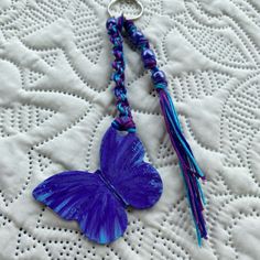 a blue butterfly keychain with tassels on it's sides sitting on a white doily