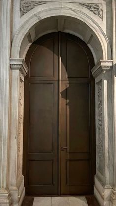 two brown doors are open in an arch with columns on either side and the light shining through them