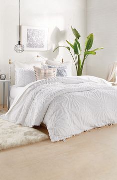 a bed with white comforter and pillows in a room next to a potted plant