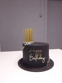 a black and gold birthday cake sitting on top of a white table with candles in it