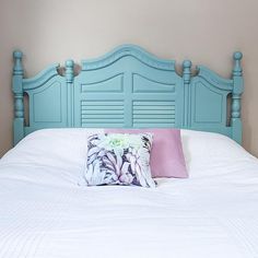 a white bed with blue headboard and pink pillow on it's side in a bedroom