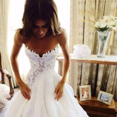 a woman in a white wedding dress is looking down at her shoes on the bed