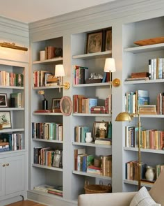 a living room filled with lots of books on top of white shelves next to a couch