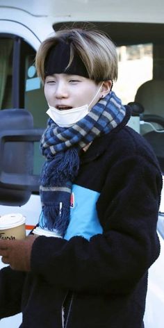 a young boy wearing a bandana and holding a coffee in front of a white van