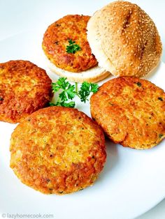 four small burgers on a white plate next to a bun and sprig of parsley