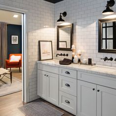 a bathroom with two sinks, mirrors and lights on the wall next to an orange chair