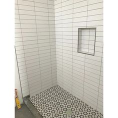 a shower stall with white tile and black and white tiles on the floor, along with a small window