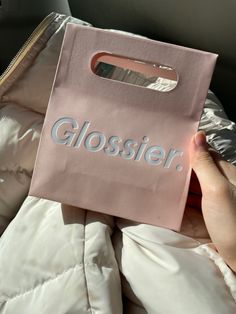 a person holding up a pink bag with the word glossier on it