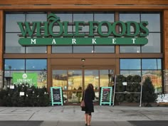 a woman is walking in front of a whole foods market building with its doors open