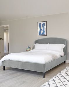 a bed with white sheets and pillows in a bedroom next to a painting on the wall