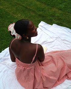 a woman sitting on top of a white blanket next to a grass covered park area