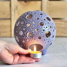 a person holding a lit candle in front of a sphere shaped object with holes on it