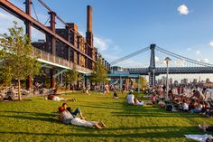 people sitting on the grass in front of a bridge