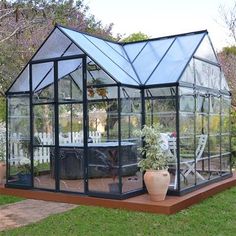 a small greenhouse with glass walls in the middle of a lawn and some potted plants