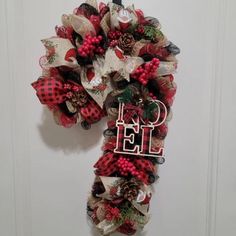 a red and white christmas wreath hanging on a door with the word noel spelled in it