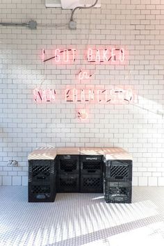 three crates sitting in front of a white brick wall with neon signs above the boxes