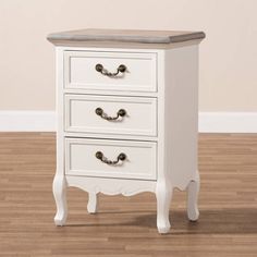 a white dresser with three drawers on top of wooden flooring next to a wall