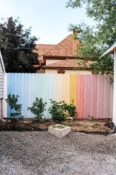 a rainbow colored fence in front of a house with gravel and rocks on the ground