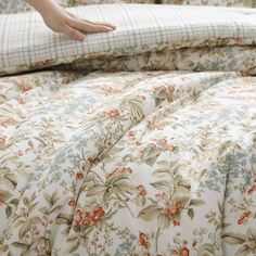 a person is reaching for the comforter on a bed with floral sheets and pillows