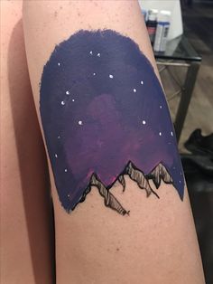 a woman's arm with a purple and black painting on it that has mountains in the background