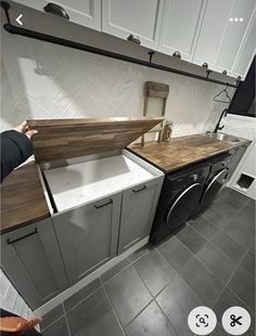 a kitchen with white cabinets and gray flooring, an open dishwasher in the middle