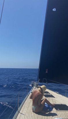 a man sitting on the deck of a sailboat in the middle of the ocean