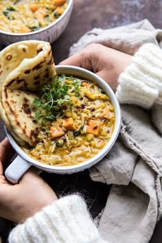 a person holding a bowl of soup with pita bread