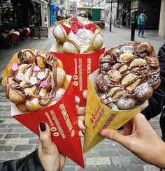 someone is holding up three cones of doughnuts with toppings on them in front of the camera