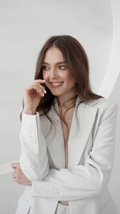 a woman in a white suit posing with her hands on her chin and looking at the camera