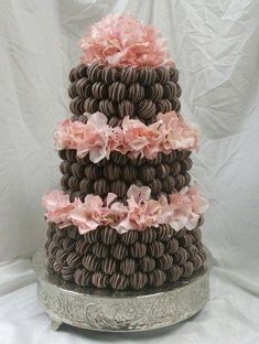 a three tiered chocolate cake with pink flowers on the top and bottom, sitting on a silver platter