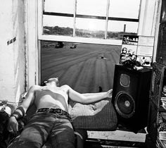 a man laying on top of a bed in front of a window next to a speaker