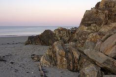 some rocks on the beach and water in the background at sunset or sunrise with pink sky