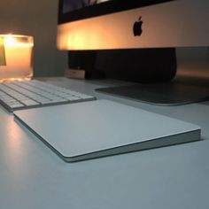 an apple computer sitting on top of a desk next to a glass of water and a lit candle