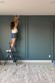 a woman on a ladder painting the walls in a room with blue and gray paint