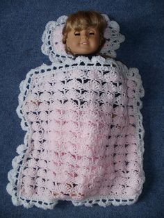 a crocheted baby blanket with a doll in it's lap on the floor