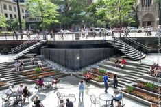 many people are sitting at tables and chairs in front of a fountain with steps leading up to it