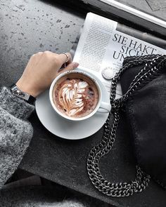 a person is holding a cup of coffee and reading the newspaper