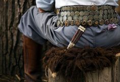 a person sitting on top of a wooden stump with a pipe in their lap and some hair around his waist