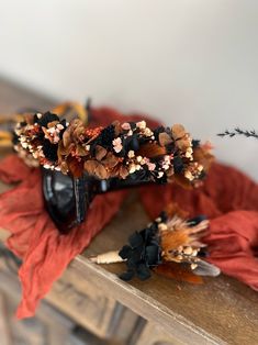 a black vase with dried flowers on top of a wooden table next to an orange scarf