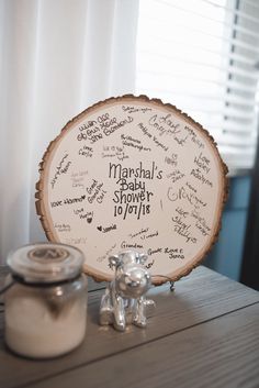 a personalized baby shower sign next to a cookie jar on a wooden table in front of a window