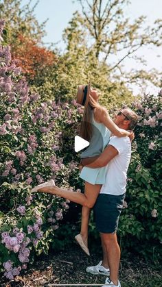 a man and woman are standing in front of some purple flowers, one is holding the other