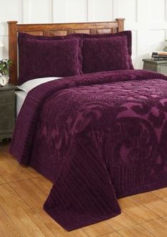 a bed with purple bedspread and pillows on top of wooden floors in a room