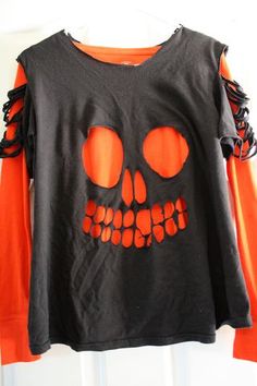 an orange and black shirt with a skull on the front is hanging from a hook