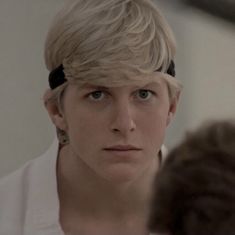 a young man with blonde hair is looking at himself in the mirror while wearing a white shirt