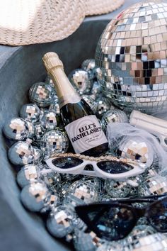 a bottle of champagne, sunglasses and disco balls are in a bowl on the table