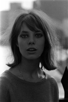 a black and white photo of a woman with short hair wearing a sweater looking at the camera