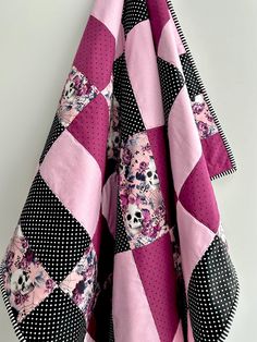 a pink and black patchwork quilt hanging on a wall next to a white wall