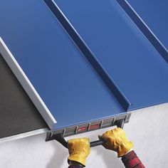 a man in yellow gloves is working on a metal roof with blue tint covering it