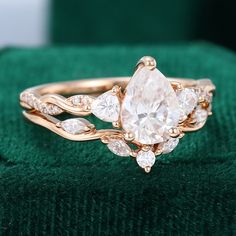 an engagement ring with two pear shaped diamonds on top of green velvet covered cushioned surface